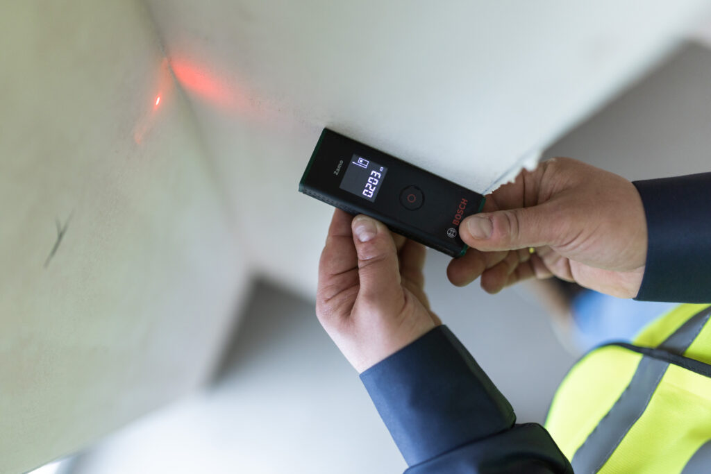 Ekspert ds. odbiorów mieszkań sprawdzający odległość za pomocą miernika laserowego. Profesjonalny nadzór budowlany i kontrola jakości wykonania nieruchomości.